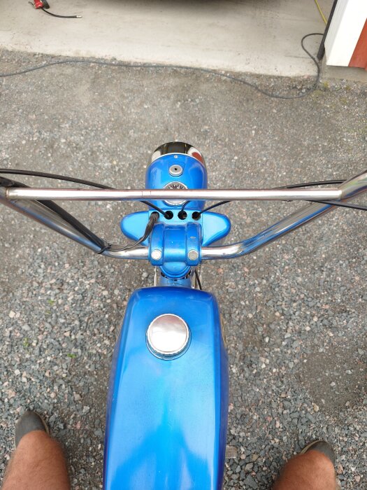 Cykelstyre och blå bensintank fångade från förarperspektiv, tanklocket glänser.