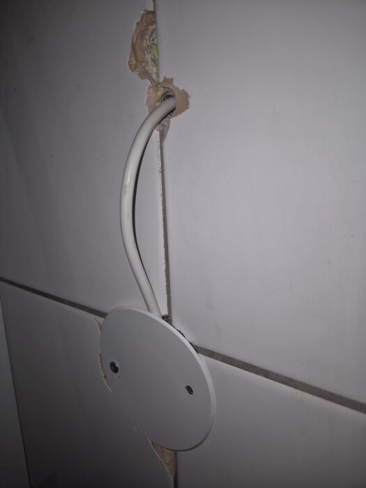 Ett hål i en kaklad vägg med ett tydligt genomdraget eluttag där kabeln syns. Rund täckplatta fäst över kabelhålet.