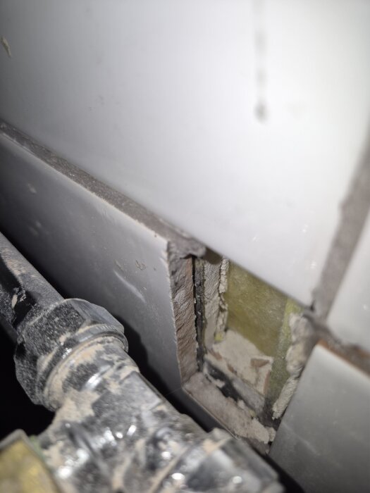 Vägg med hål och synliga rör, saknar tätskikt längre upp, eventuell eldragning bakom tvättmaskin.