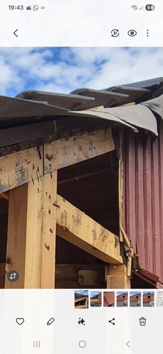 Taket och väggen på en byggnad under renovering, med synlig vindduk och panel, samt frilagda träbjälkar och himmel i bakgrunden.