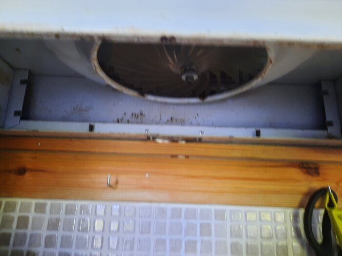 Luftventilation utan plåtar och filter, fläktblad synliga och omgivande träpanel och vägg.