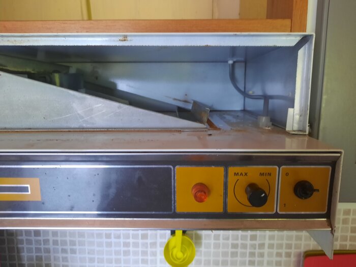 Inre delen av en köksfläkt visas, med lösa plåtar och filter borttagna, exponerar fläktens kontroller och ovansidan av köksskåp.