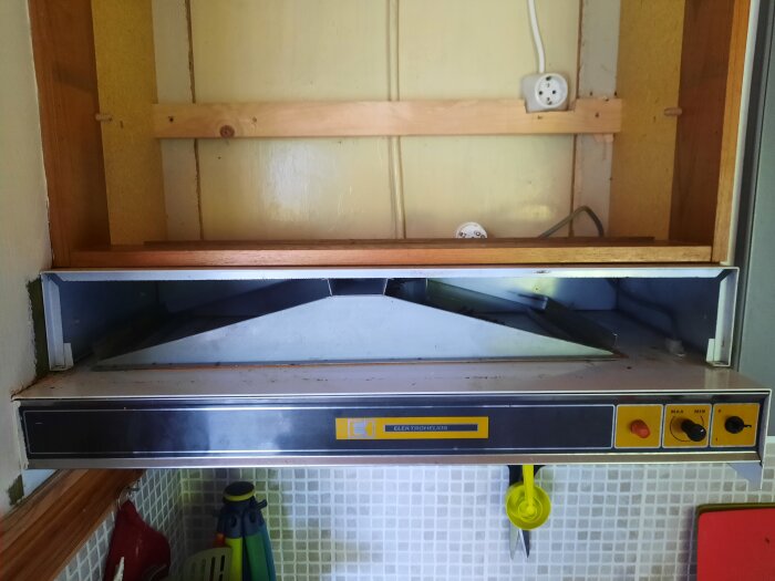 Köksfläkt utan lösa plåtar och filter, del av renoveringsprojekt, visar inre konstruktion och eluttag i bakgrunden.