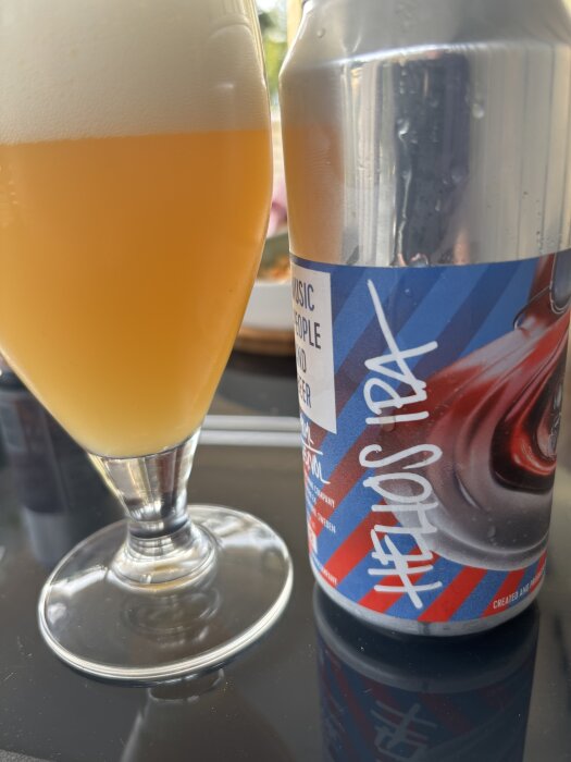 Glas med skummande Apex Helios IPA och en ölburk med etikett på ett bord.