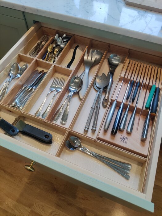 Kökslåda med hemmagjorda plywoodinsatser organiserar bestick och köksredskap, inklusive skedar, gafflar och knivar.