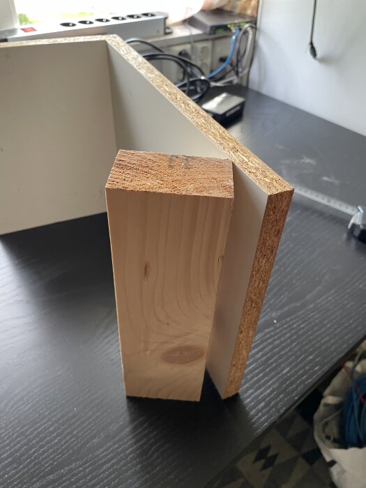 Träkloss som stöttar en melaminskiva i verkstaden på ett svart bord.