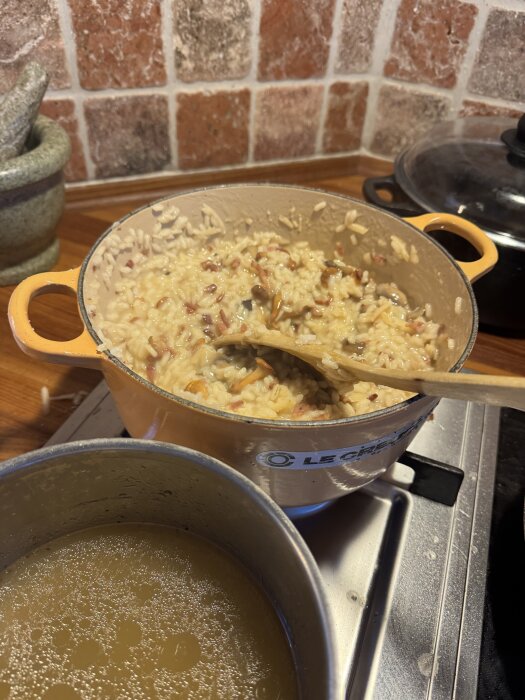 Risotto med pancetta och kantareller tillagas i en gryta, bredvid står en kastrull med kycklingfond.
