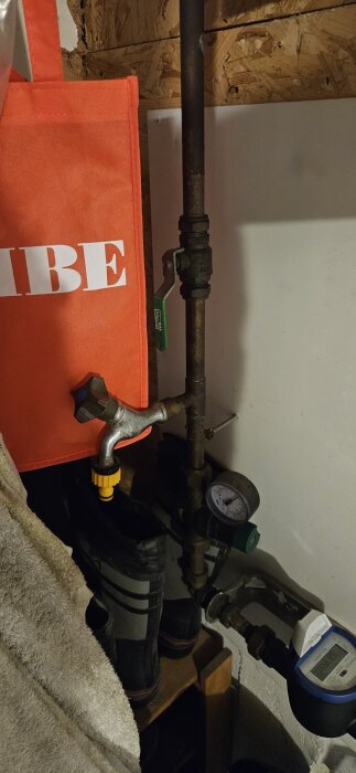 Vattenrör med ventil och vattenmätare i ett förråd, omgiven av verktyg och utrustning för trädgårdsbevattning.