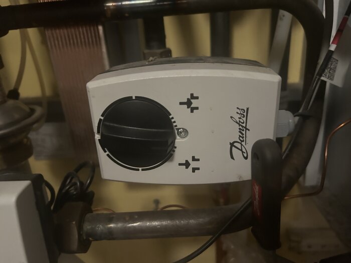 Danfoss reglerventil med vridbar svart ratt monterad på fjärrvärmecentralens rör.