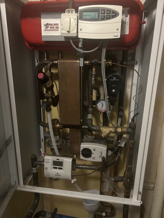 Danfoss fjärrvärmecentral med reglerventil, rör och styrpanel. Ventilen nämns i texten som ibland hänger sig vid temperaturreglering.
