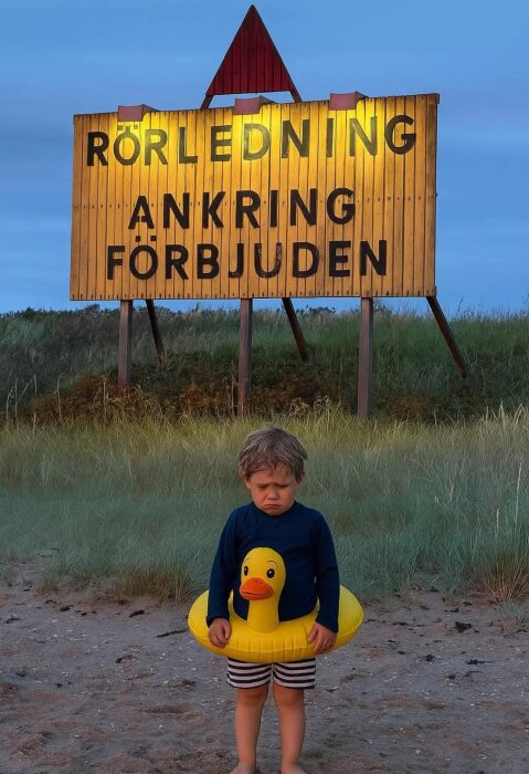 Barn med badring står ledset framför en skylt som förbjuder ankring.