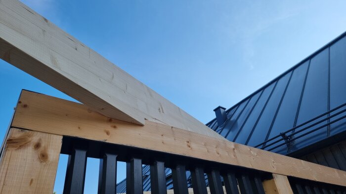 Prefab takstolar monterade på plats med ett modernt svart tak i bakgrunden mot en klarblå himmel.