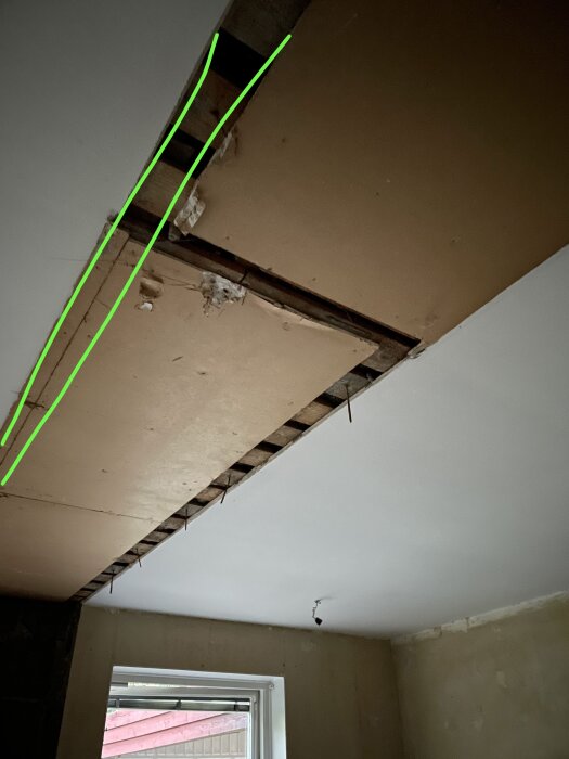 Innertak med borttagen del uppvisar synliga reglar och gröna markeringslinjer där en ny vägg ska byggas.