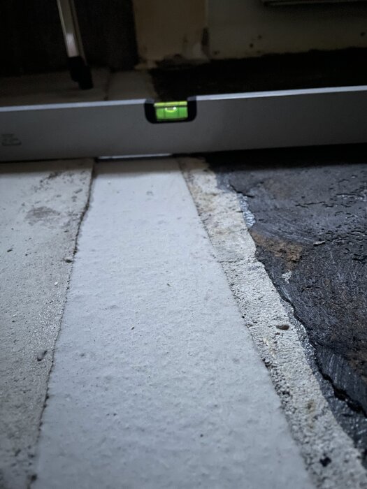 Vattenpass på golv visar nivåskillnad mellan flytspackel och gammalt golv där en garderob tidigare stod.