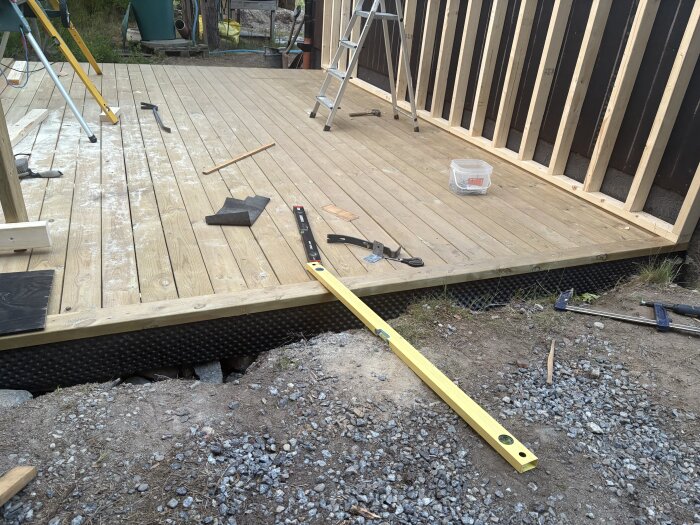 Träplattform med verktyg och byggmaterial på en byggplats för kallförråd, inkluderar vattenpass och stege.