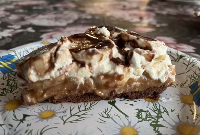 Bananoffepaj med grädde, bananer och karamell på chokladkexbotten, serverad på en blommig papptallrik.