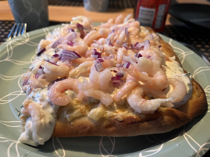 Pinsa med räkor och rödlök på en tallrik, täckt av en krämig sås.