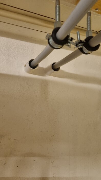 PVC-rör kopplade genom vägg, säkrade med metallfästen. Några smutsfläckar synliga på väggen och rören.