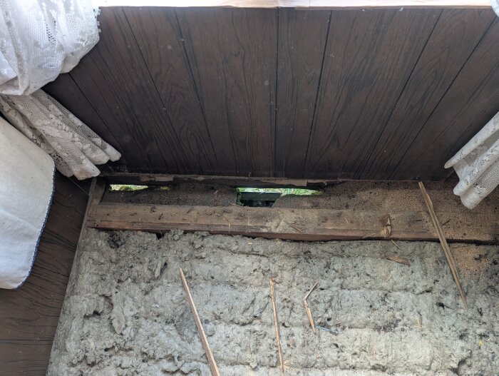 Ruttna träreglar och synlig isolering i ett hus med sättningar samt tecken på musangrepp, visar renoveringsutmaningar.