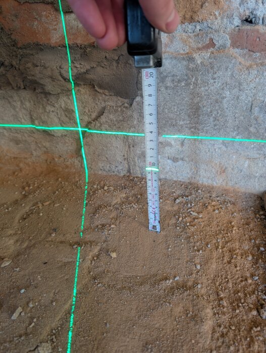 Laserlinje och måttband används för att mäta höjdskillnader på ett ojämnt golv under husrenovering.