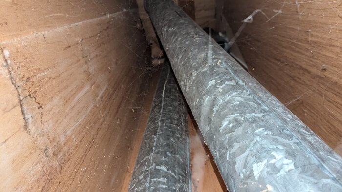 Två metallrör inuti en gammal ventilationskanal med spindelväv, varav ett rör inte är anslutet till något.