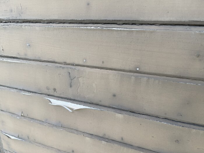 Flagnande färg på gammal garageport av trä, med synliga skador och sprickor i ytan.