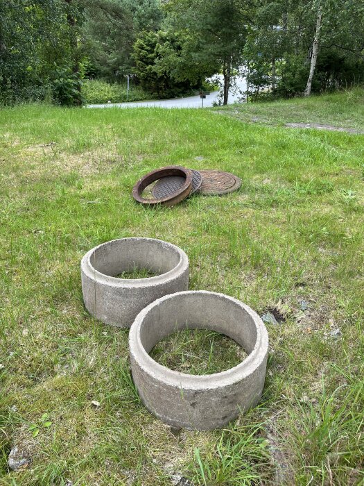 Två betongrör på en gräsmatta med skog i bakgrunden och ett par brunnslock bredvid.