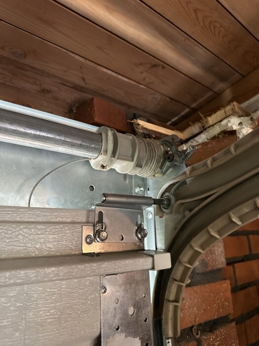 Närbild på en trasig fjädermekanism på en Wayne Dalton garageport, anslutningar och metallstruktur synliga.
