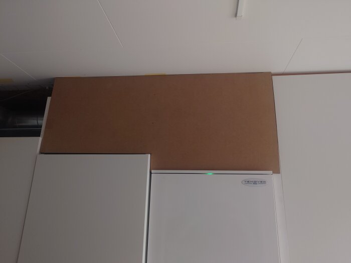 Vitt köksskåp under en bräda vid taket, märket Temovex syns på det vita skåpet.