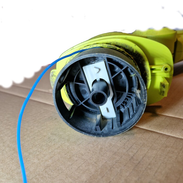 Gul trimmer med blå tråd som fastnat i spolen.