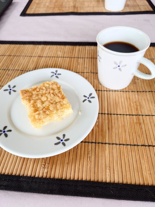 Nybakad vaniljruta på en tallrik bredvid en kopp svart kaffe på ett bord med bambuunderlägg.