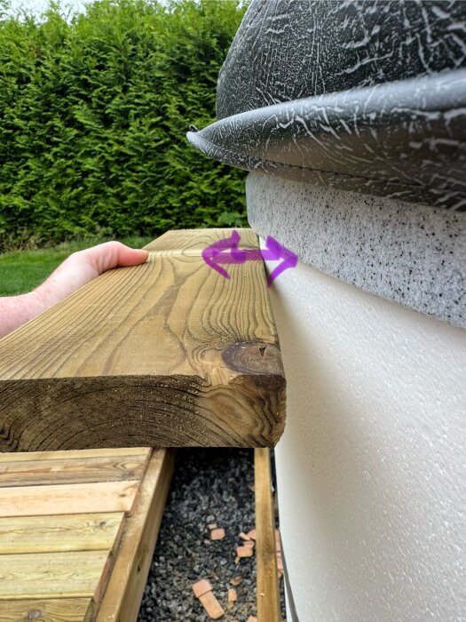 Träplanka hålls mot kant av pool, med synligt avstånd mellan trall och bad, illustrerat med lila pilar.