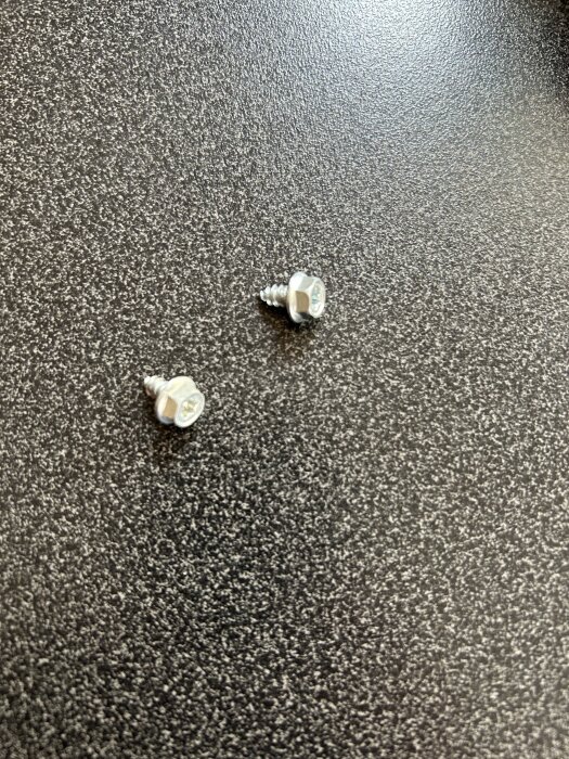 Två lösa skruvar på ett bord efter reparation av en Whirlpool diskmaskin.