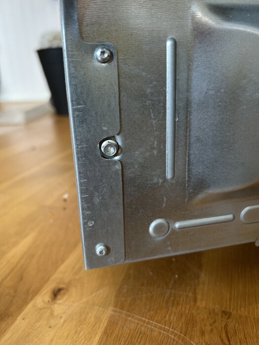 Baksidan av en Whirlpool diskmaskin med tre skruvar monterade på en metalldel, fotograferad på ett trägolv.