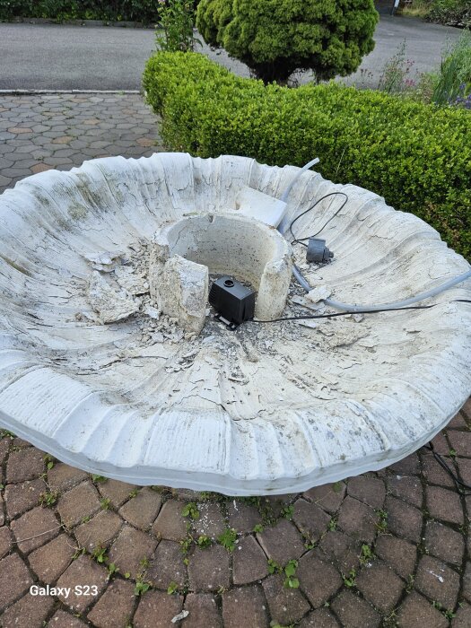 En trasig fontän med sliten yta och kablar synliga på en stenkant.