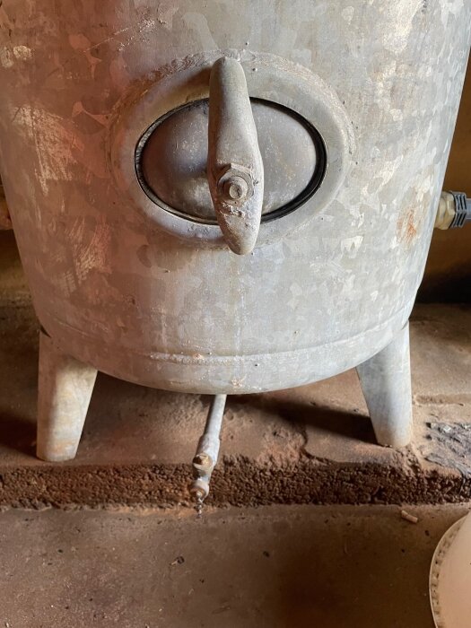 Närbild av en gammal hydrofor med ett tapprör och skruvlock i nedre delen av tanken.