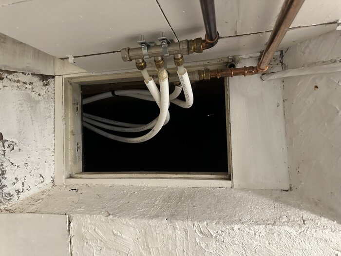 Gammalt källarfönster med installerade vattenrör som hänger i stöd, synligt kondens. Isolering runt fönstret ser misstänkt monterad ut.