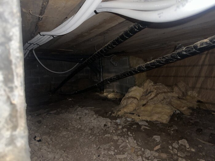 Vattenrör i källare med isolering, stöttade av rörstödet, omgiven av synlig kondens och lös isolering på marken.