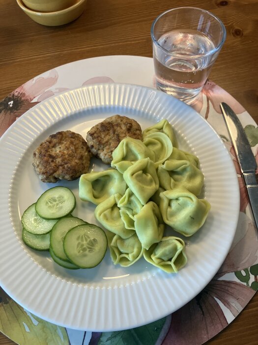 Kycklingfärsbiffar och pastakuddar med spenat och ricotta serverade med gurkskivor. Glas vatten vid sidan.