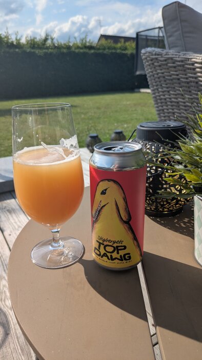 En glas öl och en burk Stigbergets Top Dawg DIPA står på ett bord i en trädgård med klippt häck i bakgrunden.