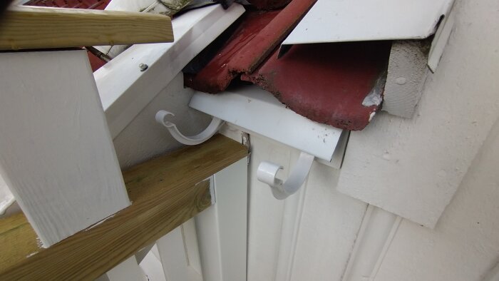 Närbild av ett vitmålat trästaket med beslag för att fästa en hängränna vid taket med röd tegel.