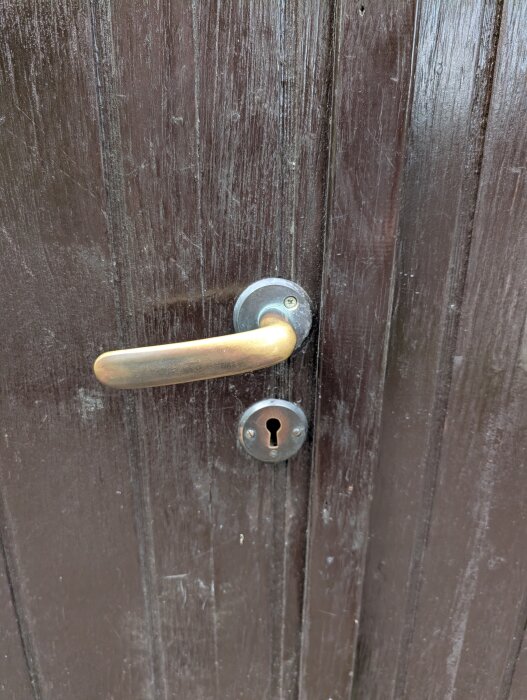 Gammal trägarageport med ett metallhandtag och nyckelhål.