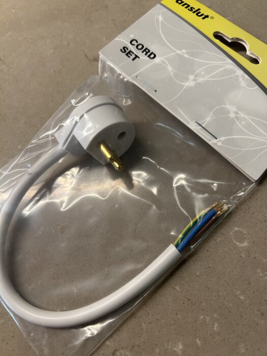 Förpackning med en vit sladd och kontakt för taklampa från Jysk, märkt "Cord Set", ligger på ett bord.