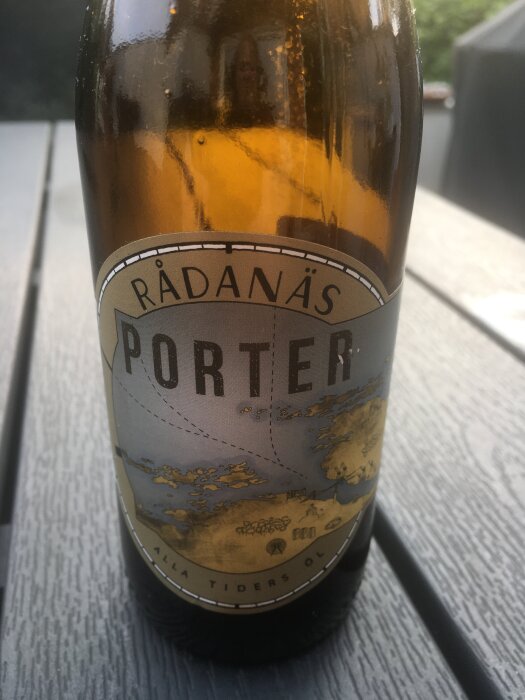 Flaska med etiketten "Rådanäs Porter" står på ett grått bord utomhus, med reflektioner synliga på glaset.
