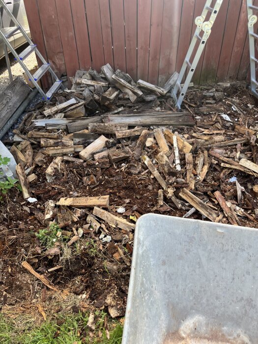Trähög och stegar vid rödfärgat plank, del av rivningsarbete för förvaring bakom uthuset.