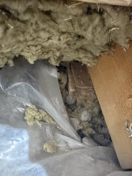 Isolering, plast, stenar och träregel under ett delvis avtäckt golv i en källare.