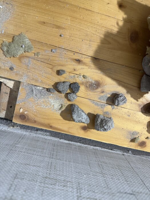 Trägolv med uppsågat hörn visar isolering och krossad sten under brädorna.