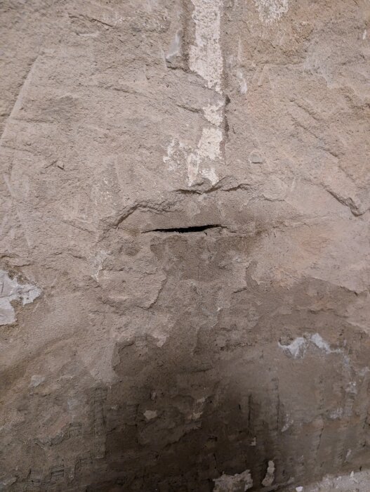 Öppet foghål i husgrundens puts, med synliga fuktmärken på omgivande yta.