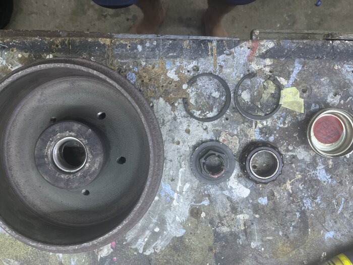 Husvagnsbromstrumma och delar av hjullager på ett arbetsbord, inklusive ringar och en burk med rödfärgat lock.