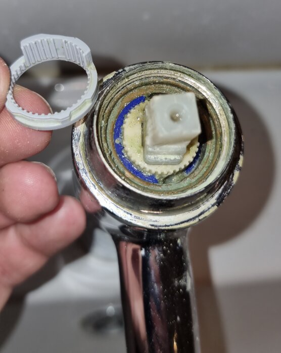 Närbild av en delvis isärplockad blandare med ett borttaget handtag och ett grått kugghjul som visas hållandes i en hand.